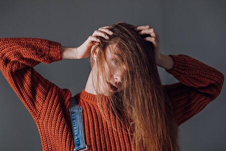 Young attractive woman in a red sweater on a gray background. Emotionsの写真素材