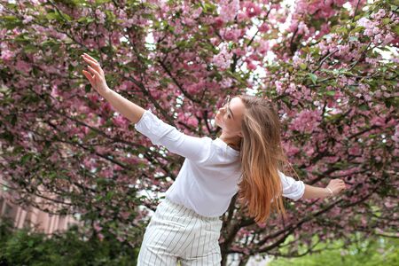 beautiful young happy woman in a blouse and glasses near the cherry blossoms. flowersの写真素材