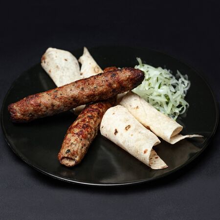 lula kebab with greens on a black plate on a black backgroundの写真素材