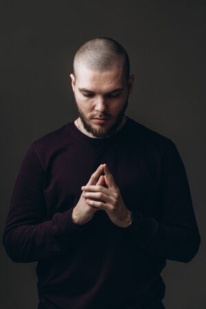close-up portrait of a serious young man looking down on gray background. bald with a beard.の写真素材