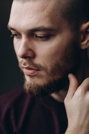 close-up portrait of a serious young man looking away on a gray background. bald with a beard.