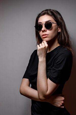 beautiful young brunette woman in black sunglasses and a black t-shirt on a gray backgroundの写真素材