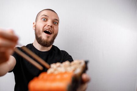 young man in a black T-shirt eats sushi rolls on a white background. isolated