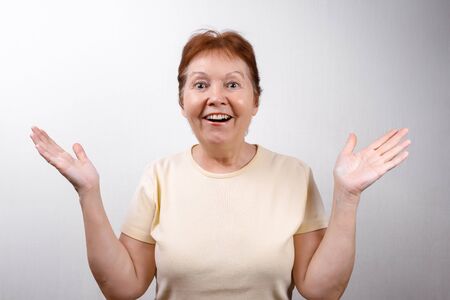 beautiful senior woman looks in surprise at the frame on a white background in a light T-shirt. emotionsの写真素材