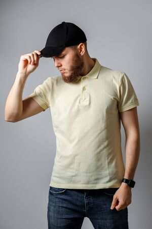 Portrait of a happy young man in a yellow T-shirt and black cap looks away on a gray background. isolated. Copyspaceの写真素材