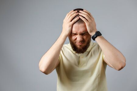 Portrait of a young upset man in a yellow t-shirt holding his head on a gray background. isolated. copyspace.の写真素材