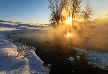 The sun breaks through the mist on the riverの写真素材