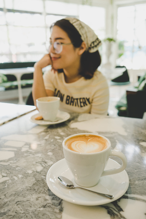 Cup of cappuccino with blurred girl drinking coffee in the cafe.の写真素材