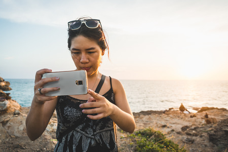 Portrait of Asian woman selfie with ocean in background in sunset scene.の写真素材