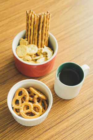 Mini pretzels in the bowl and black coffee on wooden background.の写真素材