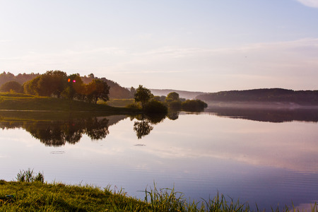 Peaceful evening near the lake in summer. Trees and sky reflection in the water. Foggy evening in the countrysideの写真素材