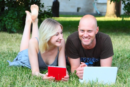 Young married couple in park with the laptop and the electronic bookの写真素材