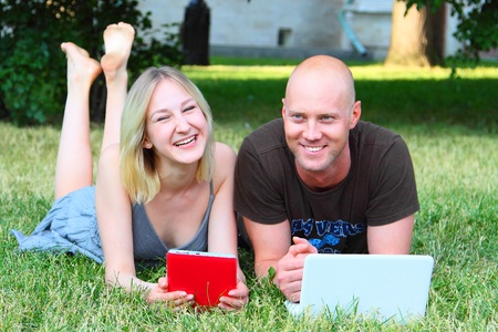 Young married couple in park with the laptop and the electronic bookの写真素材