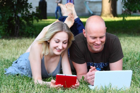 Young married couple in park with the laptop and the electronic bookの写真素材