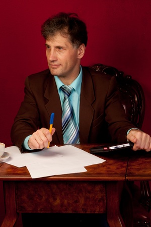 Portrait of middle-aged man working in his home at his desk on a background of red wallpaperの写真素材