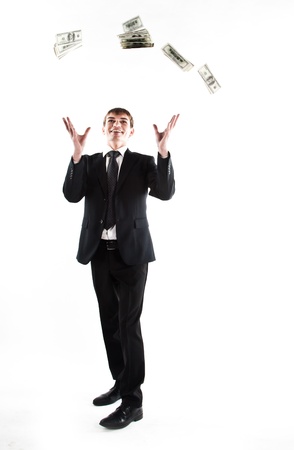 Portrait of a young businessman in a dark suit surrounded by flying dollar billsの写真素材