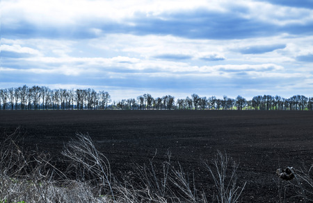 Blue sky with clouds over black fieldsの写真素材