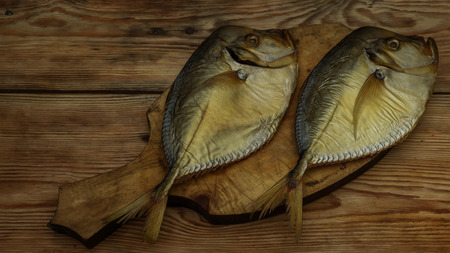 two smoked fish on a wooden cutting board closeupの写真素材