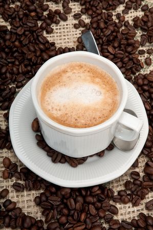 Cup of cappuccino coffee with background of coffee beans and burlap.の写真素材