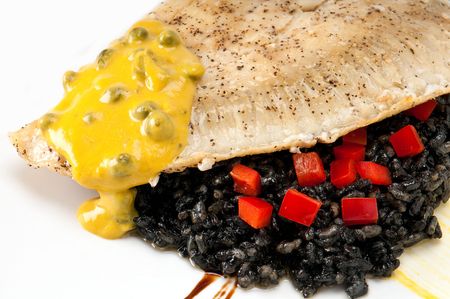 Close up of plate of halibut fillet over a bed of rice with squid ink, capers tomato and mustard.の写真素材