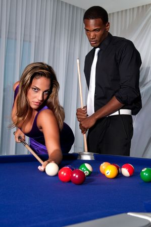 Multiracial couple playing pool at night in upscale place.