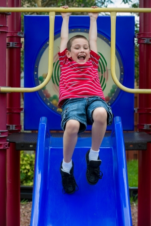 6 years old boy hanging on a slide very happy in a playground の写真素材