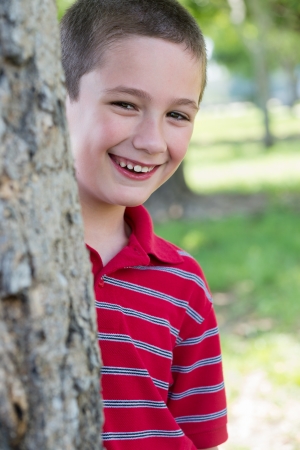Caucasian boy smiling behind a tree in a park during summertimeの写真素材