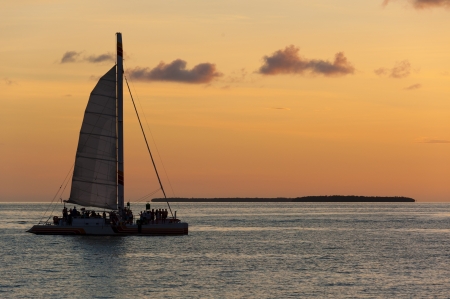 Catamaran sailing with tourists with a caribbean island behind at sunset の写真素材