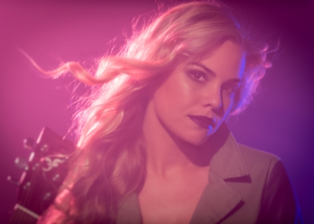 Blonde woman holding electric guitar over the purple backgroundの写真素材