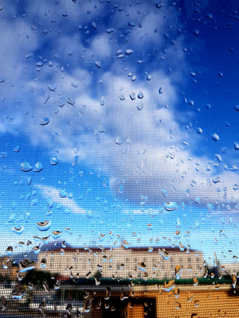 raindrops on the window with blue sky and white clouds in the background