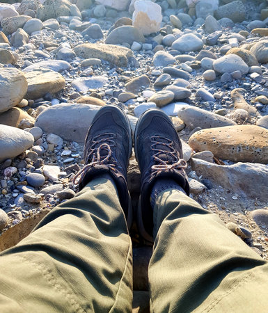 Close-up of male legs in hiking boots on pebble beachの写真素材