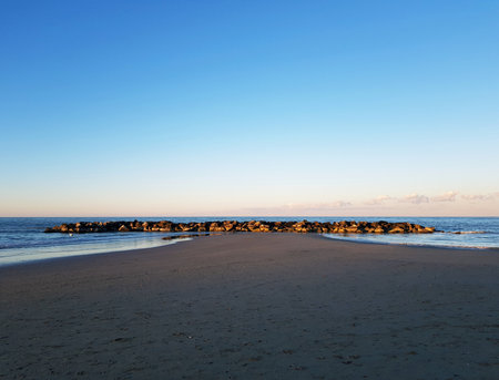 sunset on the beach with rocks and blue sky in the backgroundの写真素材