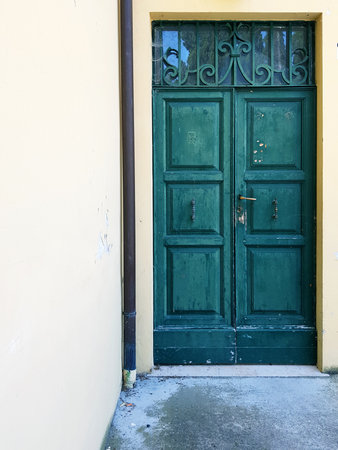 Old wooden door with green paint and white wall in the background.の写真素材
