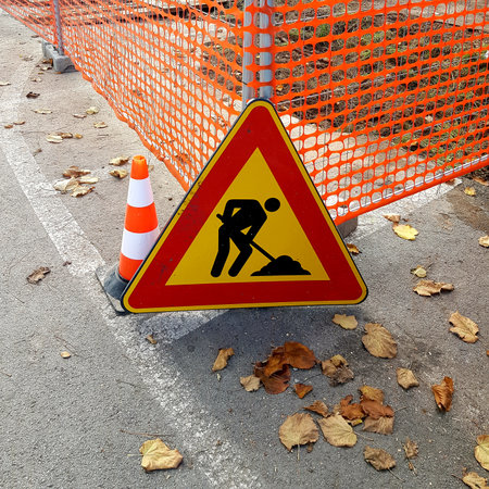 Under construction sign on the road with fallen leaves in the background.