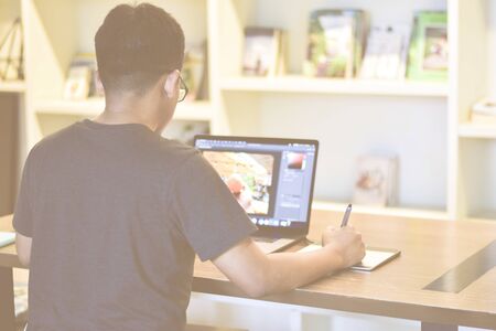 Male photographer is editing his photo using laptop and drawing pad inside cowering space/coffee...
