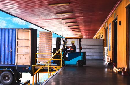 Forklift stuffing-unstuffing pallets of cargo to container on warehouse leveler dock.