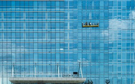 Worker inspecting glass window installation of tall glass exterior office building. Tall glass building cleaning. Working at high safety.の写真素材