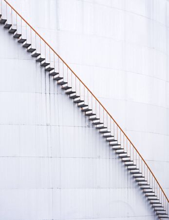Spiral metal stairway climbing up white storage tank at oil and gas tank field.の写真素材