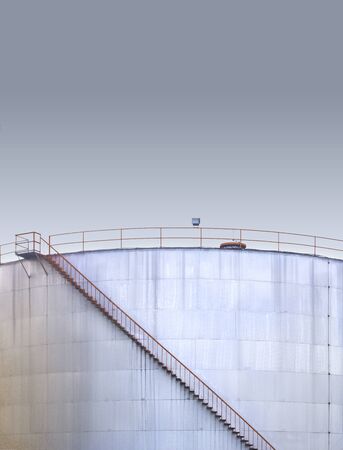 Spiral metal stairway climbing up white storage tank at oil and gas tank field.の写真素材