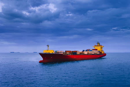 A large red container ship in the open sea with dark clouds background. Shipping, Import, Export, and Logistics concept.の写真素材