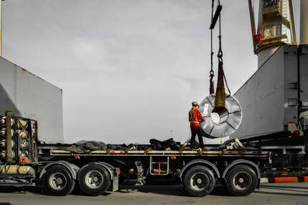 Ship crane put away steel coil on the trailer, worker stands on truck placing coil on the support skit.の写真素材