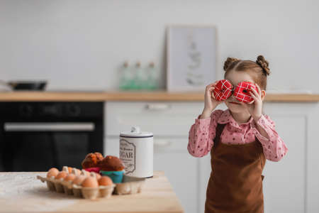 little girl in the kitchen laughs and looks through a round pink donuts