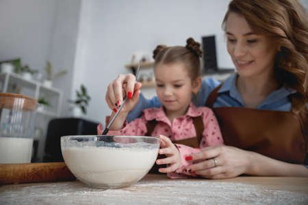mom and daughter in the kitchen have fun and cook food from flour, milk and eggsの写真素材