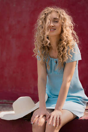 girl in a blue dress sits on a red building and smilesの写真素材