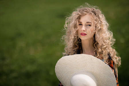 girl with curly hair holds in her hand a large round white hat on nature