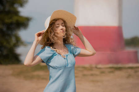 girl in a blue dress and a big straw hat outdoors enjoys the sunの写真素材