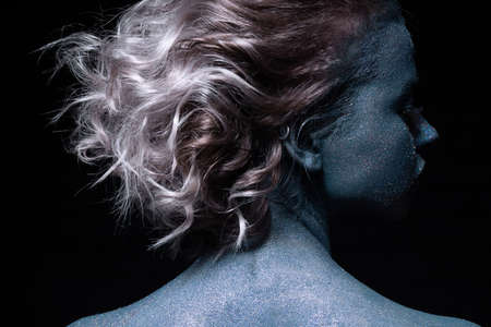 girl with a blue face in sparkles close-up against a black wall looks at the cameraの写真素材