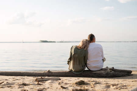 man and woman are sitting on a log by the sea and looking into the distanceの写真素材