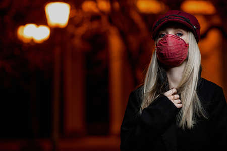 a girl in a black coat and in a red mask walks around the city at nightの写真素材