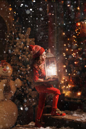 little girl in a sweater and a hat carries a big lantern on a snowy streetの写真素材